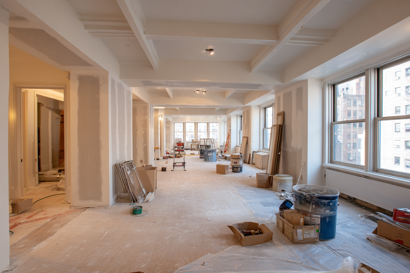 Close-up of exposed structural beams and plumbing during a high-end NYC renovation, blueprint resting nearby.
